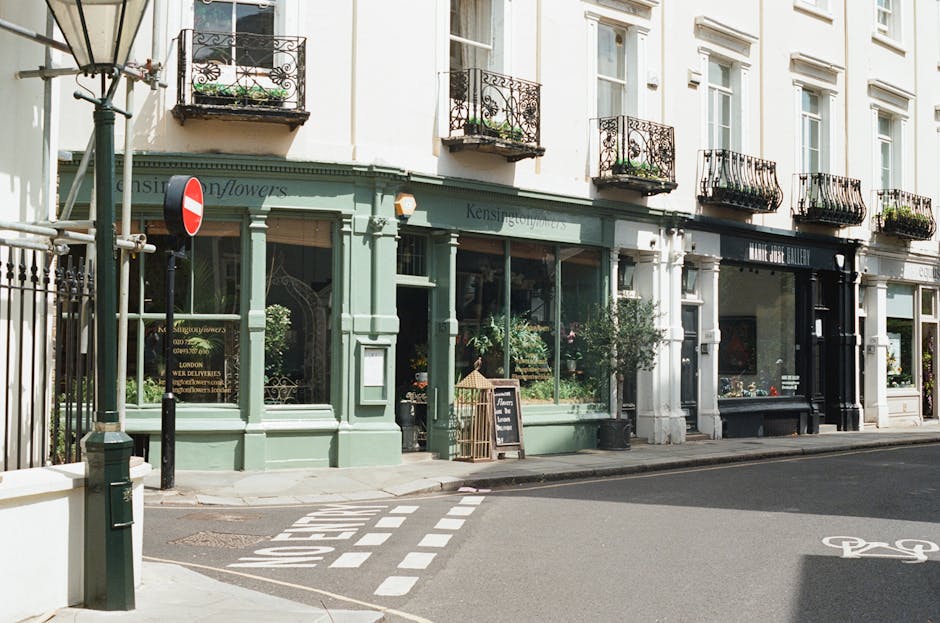 The exterior of a floral shop on Croydon Road Elmers End featuring a light green painted storefront with large display windows showcasing various flowers. The shop's name, partially visible, is on a s
