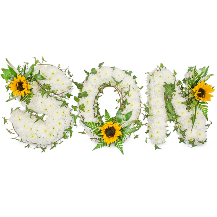 A carefully constructed, three-dimensional sympathy tribute spells the word SON in large capital letters, each letter formed from a compact, even mattress of pristine white chrysanthemums whose small heads create a fine, textured surface across the face of the letters. Winding through the chrysanthemum base are strands of dark green ivy, their glossy, lobed leaves and slender stems interlacing the white blooms to add structural rhythm and a living, evergreen underline. Lighter green fern fronds and pointed foliage emerge strategically to break the white fields and lend sculptural contour. Three bold sunflowers anchor the arrangement: one placed at the upper-left curve of the S, another positioned at the lower center of the O where it sits amid a cluster of fern fronds, and a third set on the upper-right limb of the N. Each sunflower's broad yellow petals radiate outward from a textured dark brown disk, creating warm visual counterpoints that draw the eye across the composition. The piece was photographed against a stark white background with directional, soft lighting that emphasises the depth, shadow and tactile quality of the florals while keeping the overall mood restrained and reverent. This personalised tribute reads as a dignified funeral or memorial arrangement for a beloved son - pairing classical white bereavement flowers with cheerful sunflowers and varied greenery to suggest both sorrow and consolation, making it appropriate for wakes, remembrance services or display at a graveside in and around Elmers End and nearby Croydon.
