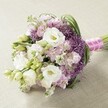 A sumptuous hand-tied bouquet, artfully arranged upon a neutral, subtly textured beige surface, reflects the refined taste of Elmers End's weddings and special events. The arrangement showcases large, ruffled white Lisianthus flowers at its core, their creamy centers and silky petals drawing the eye. Around them, clusters of pastel pink and lavender Stock blossoms create ruffled, cloud-like bouquets, lending depth and soft colour. The unique character of the bouquet is elevated by bold deep purple Allium 'Star of Persia', their spiky, spherical forms bringing striking texture and modern flair. Slender green leaves and bright Lisianthus buds weave throughout, invoking the vitality of Elmers End's local gardens and parks. The bouquet is finished with a vibrant fuchsia satin ribbon binding the stems, topped with a string of delicate white pearls for sophisticated sparkle. Illuminated by gentle, even lighting, the flowers radiate their natural beauty and harmonious colour palette. Whether intended as a bridal bouquet or a centerpiece for a celebration at Elmers End Green, this floral arrangement exudes timeless romance, craftsmanship, and the fresh creativity you expect from your neighbourhood florist.